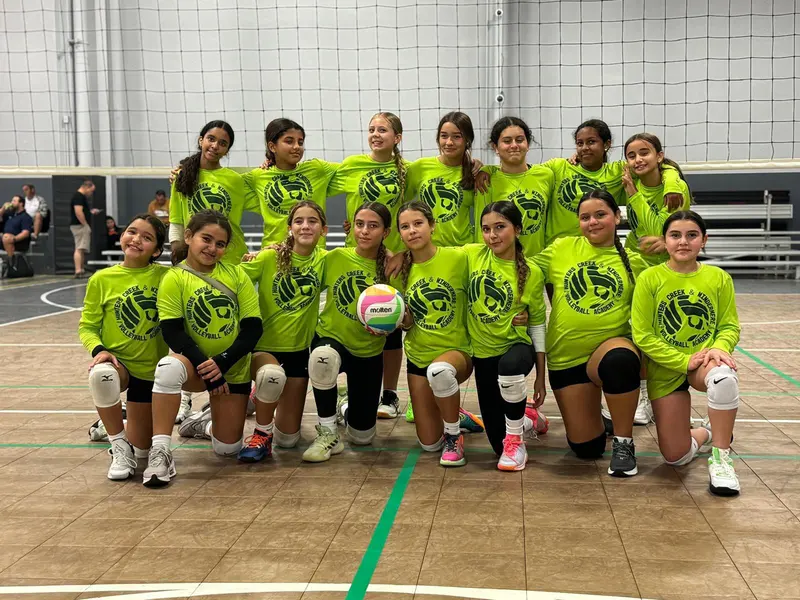 Hunters Creek Volleyball Academy team in bright green shirts kneeling together on a court